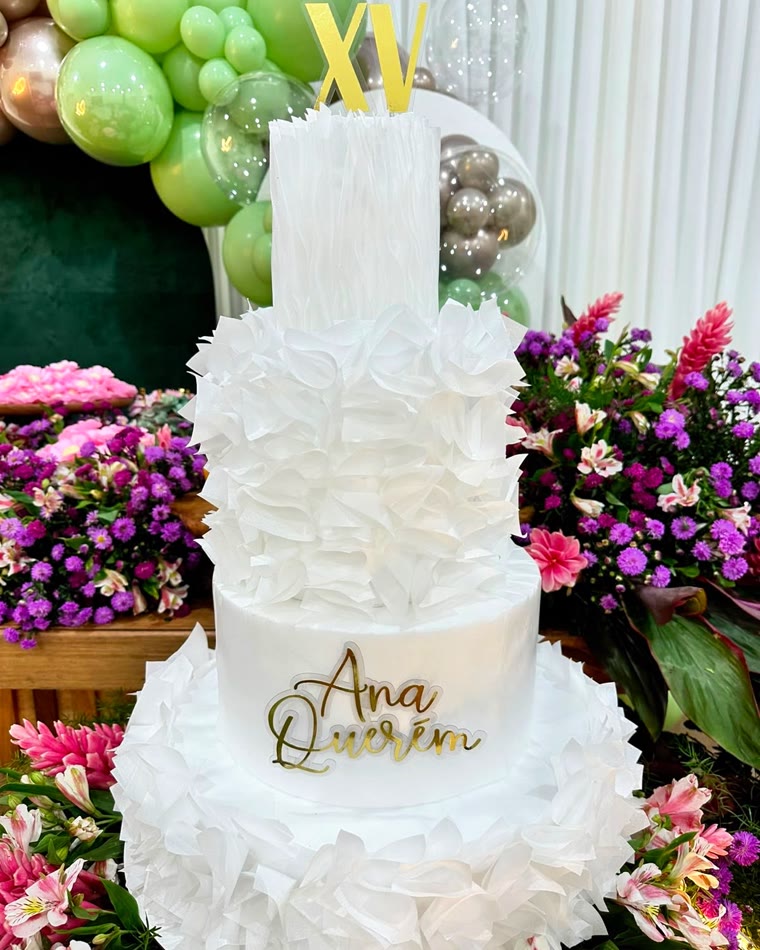 Bolo de 15 anos branco de vários andares, cercado por arranjos de flores