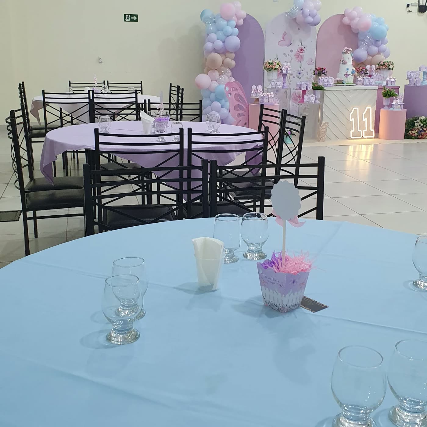 Mesas em tons pastel e a decoração de aniversário ao fundo