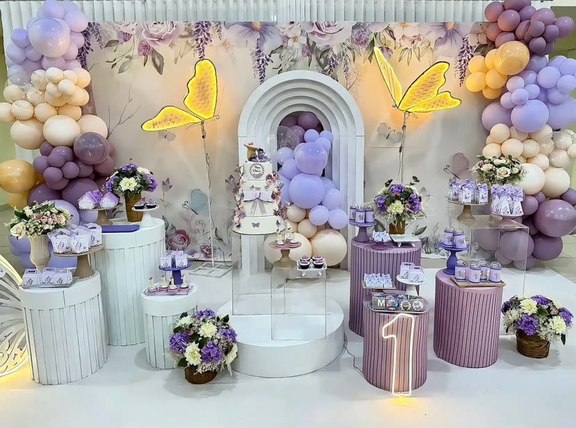 Decoração em tons de lilás, com arcos e mesa de doces