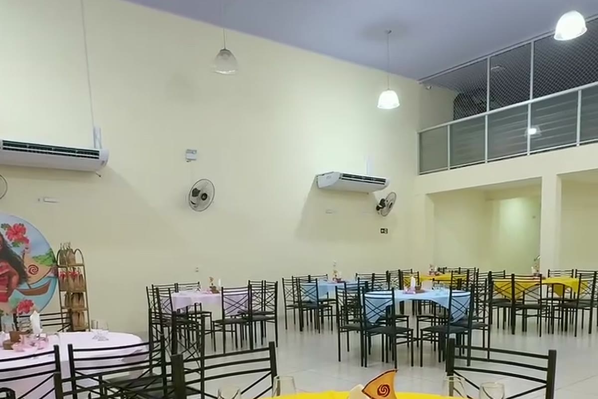 Vista ampla do salão com pé-direito alto, mezanino, ar-condicionado e mesas redondas postas